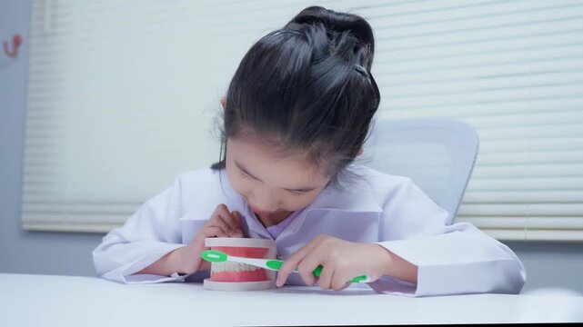 Young girl student brushing dental model practicing oral hygiene technique during anatomy class at school desk