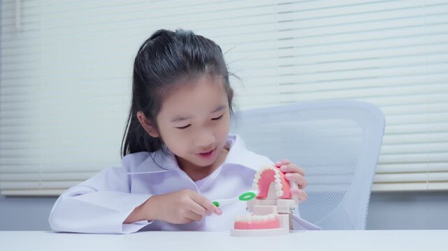 Little girl practicing dental hygiene brushing teeth on dummy model for oral health education at dental clinic