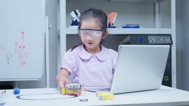 Asian girl student programming robotic arm with laptop in stem education classroom, engaged in coding and engineering project for technology development and youth innovation learning