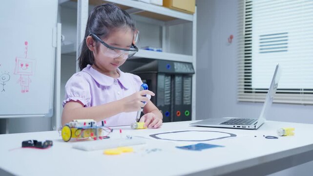 Asian girl child student assembling educational robotics kit with screwdriver at classroom desk for stem learning activity
