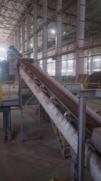 Inclined belt conveyor moving crushed red clay inside a brick factory