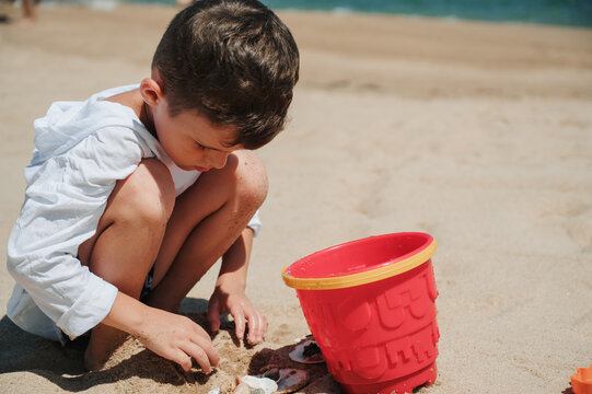 Happy child playing with sand at the beach in summer