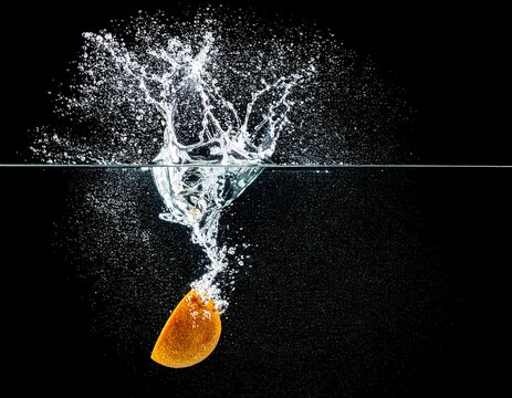 Fresh orange slice splashing into clear water on a black background, dynamic food photography with copy space
