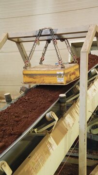 Magnetic separator hanging above a conveyor belt carrying red clay at a brick factory