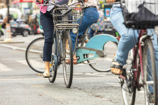 Urban cyclists riding bicycles with front baskets through city traffic, illustrating bike sharing, active transportation, sustainable mobility, and everyday commuting