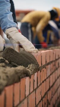 Bricklayers laying a brick wall with mortar and a trowel at a construction site