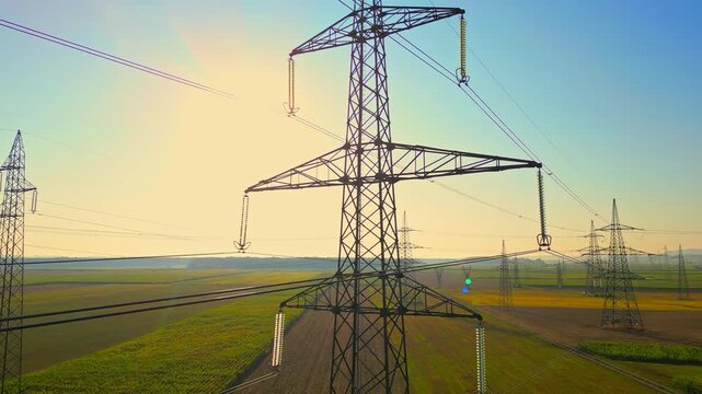 Power lines stretch across a green landscape under the setting sun, symbolizing the reliable power supply essential for modern living.
