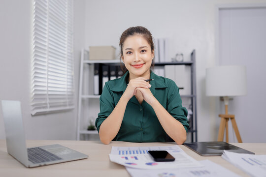 Asian businesswoman working at her desk, reviewing financial reports and documents in a modern office environment.