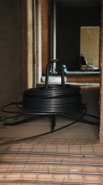 Coil of black pipe on a stand above underfloor heating pipes in a building under construction
