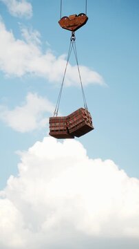 Tower crane lifting a pallet of bricks against a blue sky with clouds