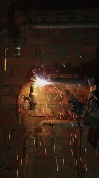 Welder joining a steel pipe on a brick wall with bright sparks indoors