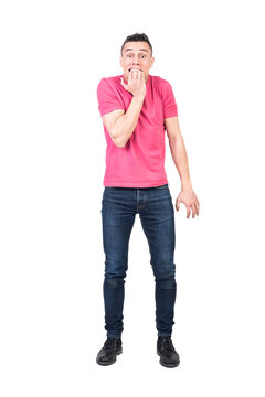 Full body of young nervous male with dark hair in t shirt and jeans biting nails and looking at camera