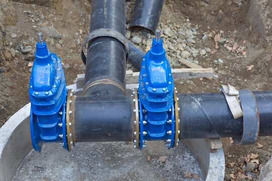 Two blue gate valves installed on steel pipeline branch inside concrete manhole base
