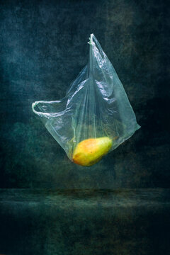 Ripe pear in a cellophane bag on a string on a dark background