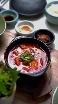 Spicy Korean tofu stew with green onion in black pot served with rice and side dishes.