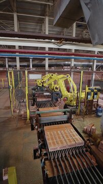 Robotic arm stacking clay bricks on a production line at a brick factory