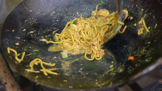 Stir frying yellow noodles with egg in hot smoking wok.