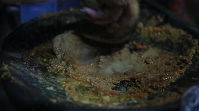 Grinding spicy ketoprak sauce using a stone mortar and pestle at the night market.