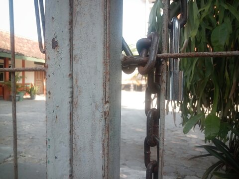 Old padlock and metal chain securing the entrance gate of a building in a rural area of Java, Indonesia, representing security, protection, access control, and restricted entry.