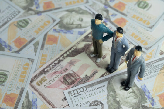 Miniature businessmen figures standing on scattered US dollar bills. Concept of business investment, human resources payroll, corporate finance, investor team, and wealth management.