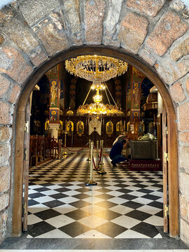 Interior view of Greek Orthodox church through stone archway with ornate golden chandelier and frescoes, Nea Makri, Greece.
