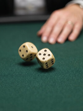 Two dice rolling on a green felt table with a hand in the background  