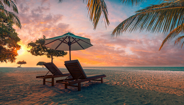 Romantic sunset tropical beach umbrella loungers palm trees pastel glowing sky calm sea sandy shore summer paradise. Perfect summer vacation travel scene. Luxury honeymoon couples relax sunset getaway