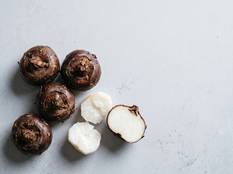 Whole water chestnuts with sliced pieces on light surface
