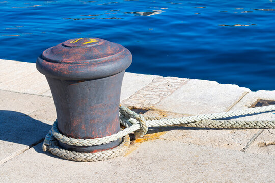 A rusty bollard sits on a concrete dock overlooking a blue bay in Rijeka, Croatia