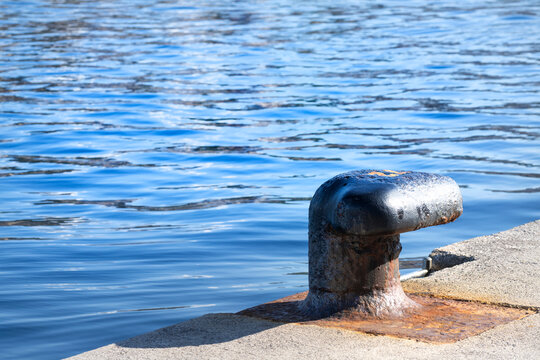 A rusty bollard sits on a concrete dock overlooking a blue bay in Rijeka, Croatia