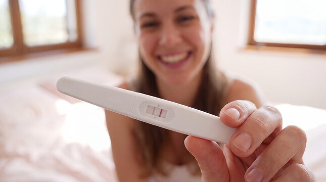 Pregnancy test positive woman happy announcement fertility conception motherhood bedroom A smiling woman shows a positive test toward camera for pregnancy reveal and family announcement campaigns