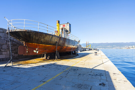 A rusty ship rests on dry dock on a sunny day in Rijeka, Croatia