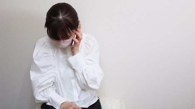 咳や発熱の症状があるマスクをした女性　電話をかける様子