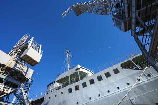 a low-angle view of a gray ship docked next to industrial cranes in the harbor of  Rijeka, Croatia
