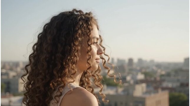 Woman with Beautiful Curly Hair Enjoying a Gentle Breeze on a Rooftop