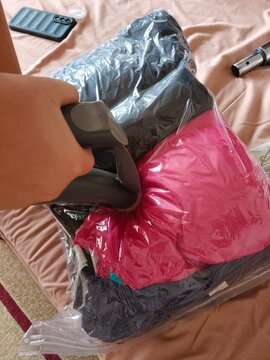 Vacuum Sealing Clothing for Moving and Household Storage. Clothing and personal belongings are being compressed inside a plastic vacuum storage bag using a vacuum cleaner. The technique reduces