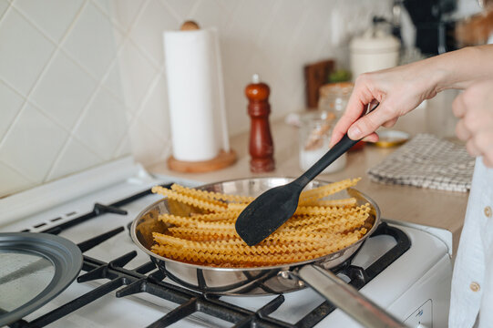 Cooking Italian pasta boiling in a stainless steel pot on a modern kitchen stove, home culinary preparation concept