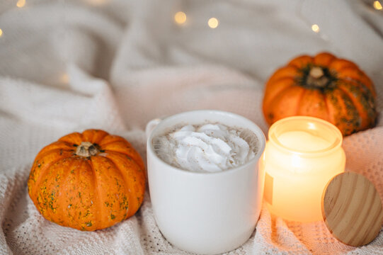 Mug of hot cocoa topped with whipped cream served with autumn pumpkins and a cozy throw blanket, warm seasonal drink