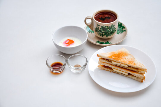Kopitiam breakfast set, kopi susu (torrefacto coffee with condense milk), soft boiled egg served with pepper and soy sauce, and kaya toast, served at a white top table