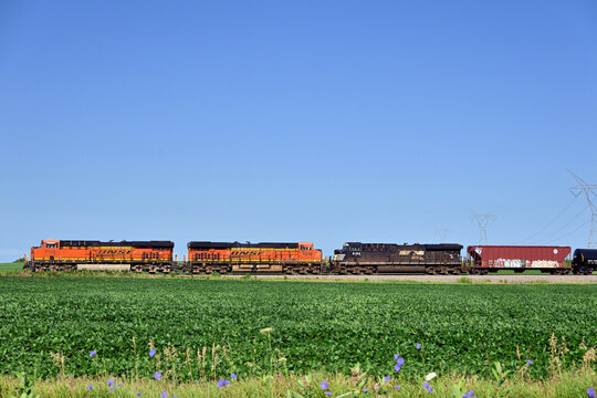 A Burlington Northern Santa Fe freight train, led by a pair of BNSF locomotives and a single Norfolk Southern unit, rumbles through the north central Illinois countryside dominated by agriculture.