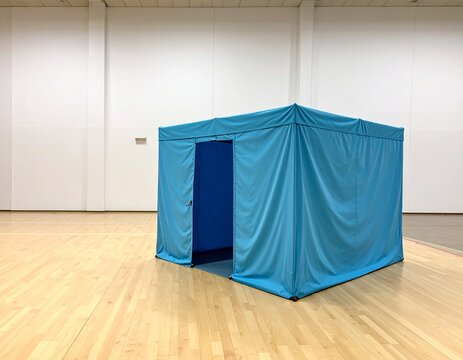 Blue fabric privacy partition tent set up in an empty evacuation shelter