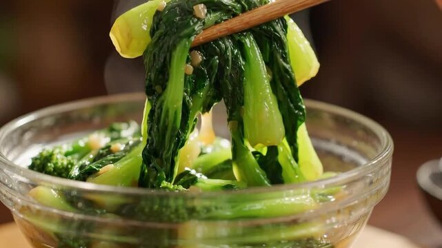 Chopsticks Picking Up Stir-Fried Bok Choy and Greens from Glass Bowl