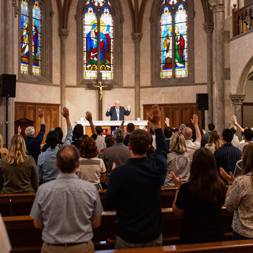 Dramatic Lighting Church Youth. A Community Gathers For A Worship Service, Singing And Praying With Uplifted Hands In Church On Easter Or Sunday Before The Cross
