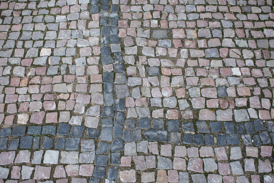 An old stone pavement made of natural cobblestones featuring shades of gray, pink, and blue. Detailed paving texture; an atmospheric urban backdrop for architectural and design projects. Background.