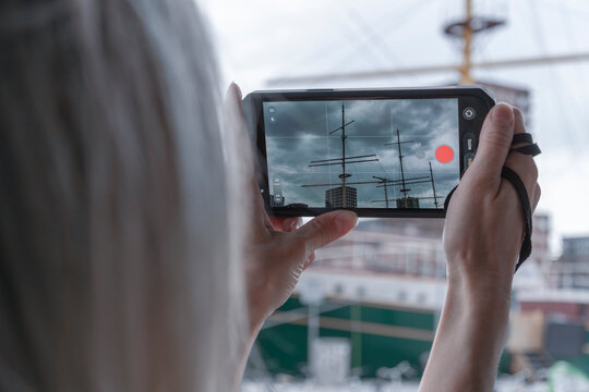 Person photographing ship masts on smartphone screen Person holding modern smartphone and taking picture of historic ship masts and harbor structures on camera screen