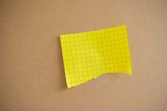 Yellow grid paper with a torn bottom edge creating a blank memo or reminder space on a textured brown surface