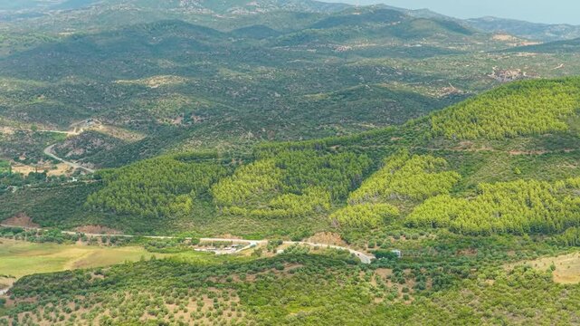 Aerial view of the rolling green hills and dense forests of the Toroni area in Halkidiki, Greece. The landscape features a mix of pine forests, scattered farmland, and winding rural roads
