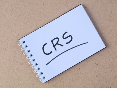 CRS text handwritten on a spiral book placed on a brown wooden texture background, representing corporate responsibility, business concept, or social initiatives