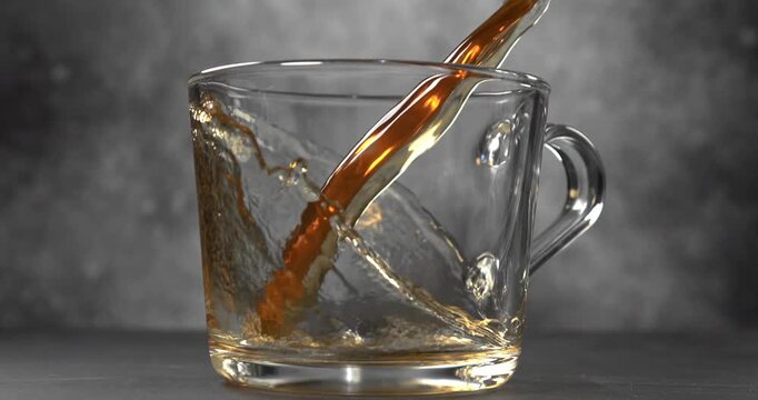 Hot tea pouring into glass cup slow motion