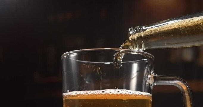 Beer pouring from glass bottle into mug in slow motion